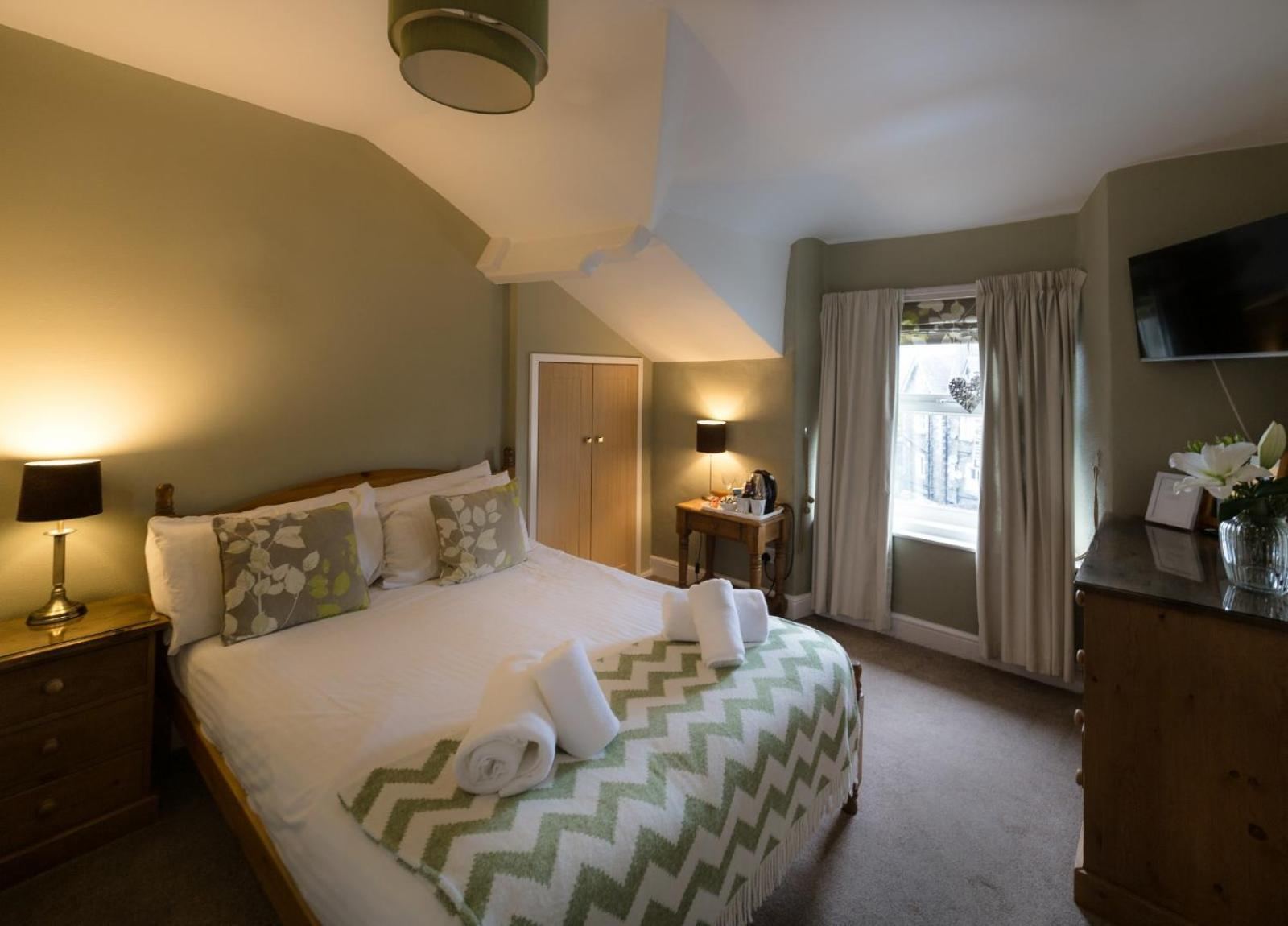 Double room with sage green walls, sloped ceiling, green and white chevron throw, wall-mounted TV and tea tray
