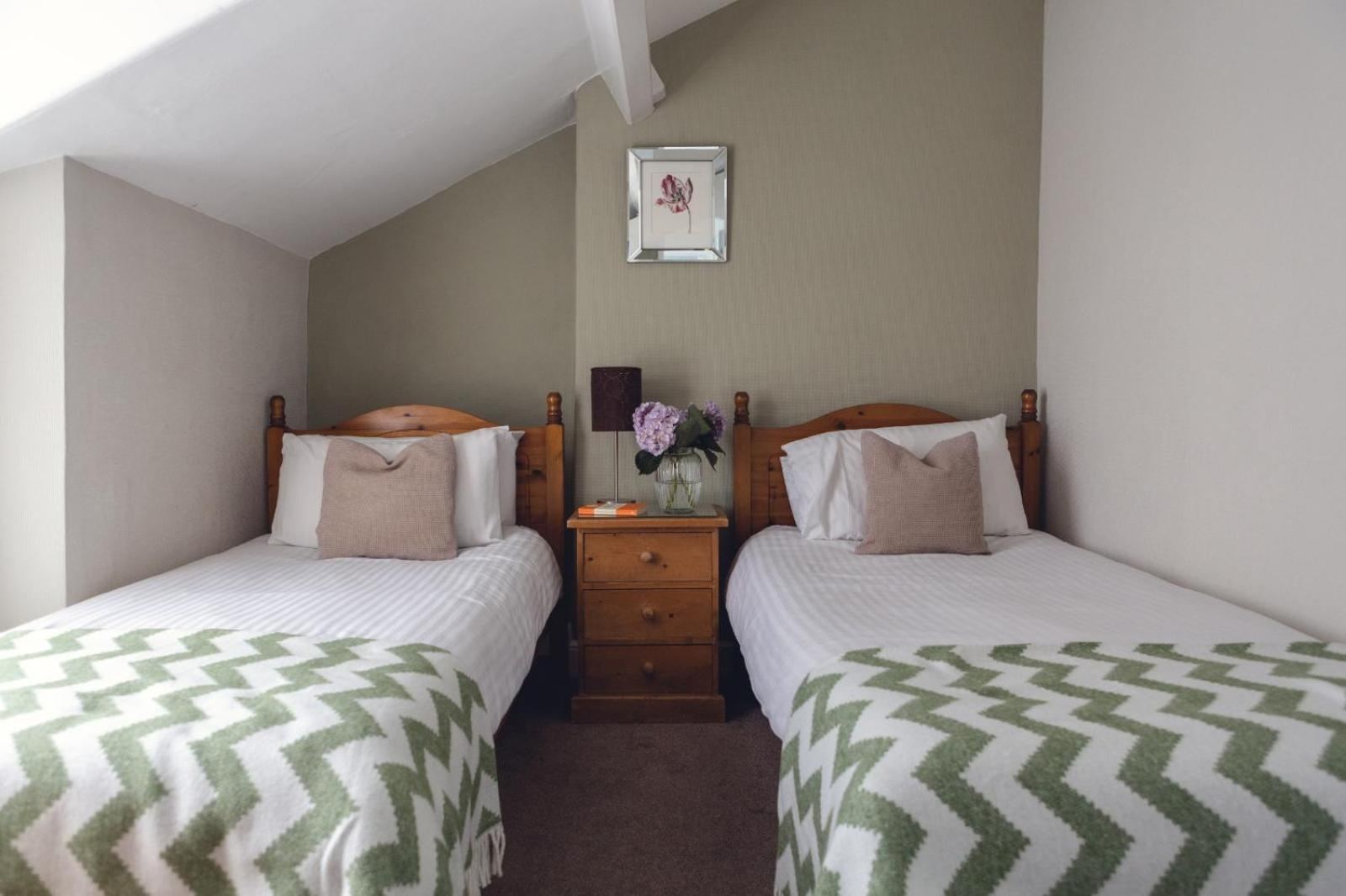 Twin room in the attic with two single beds, sloped ceiling, green and white chevron throws, hydrangeas on the bedside table