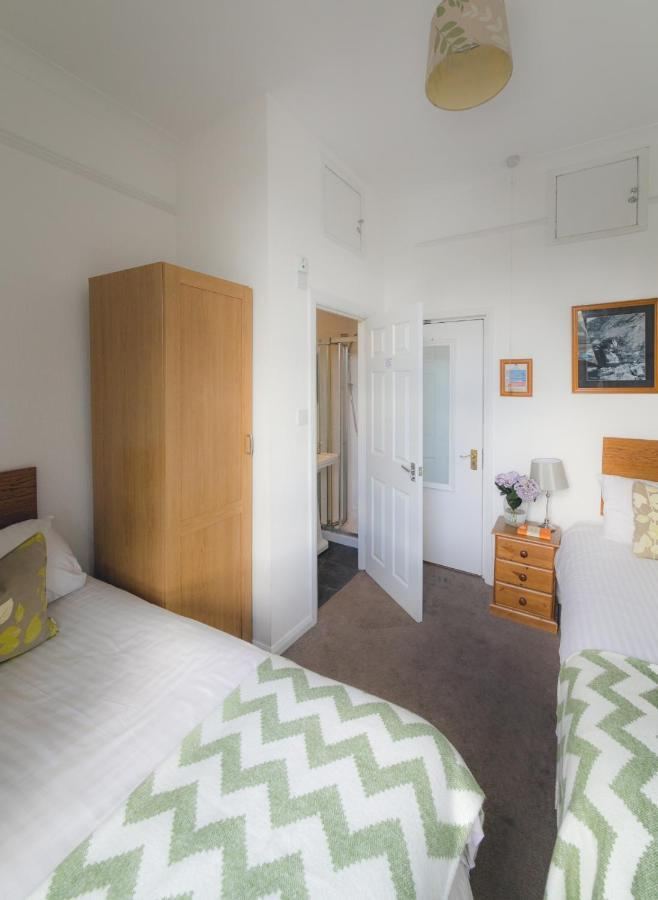 Twin room with white walls, two single beds, chevron throw, open door to en-suite bathroom